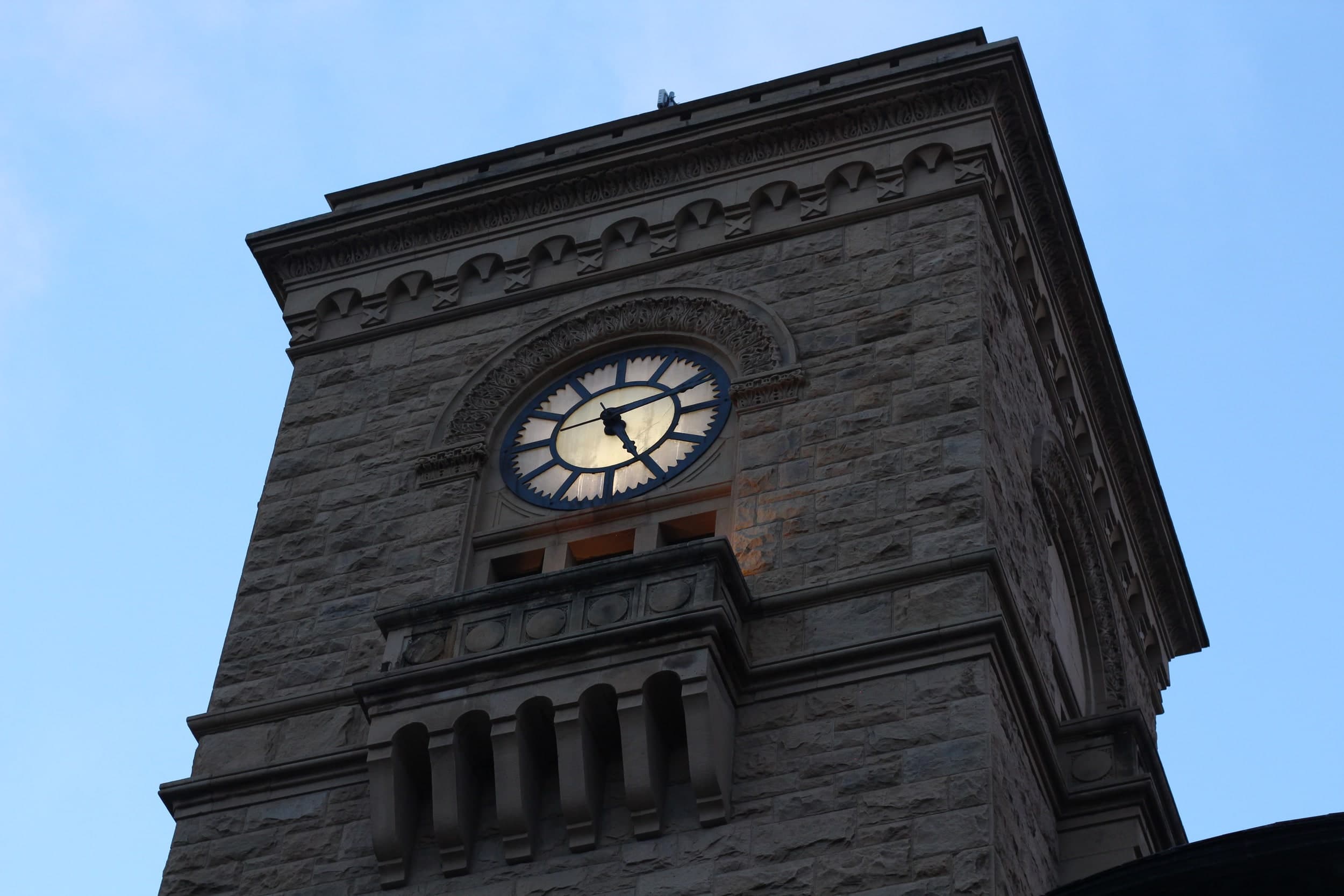 A stone clock tower with an illuminated clock face against a blue evening sky