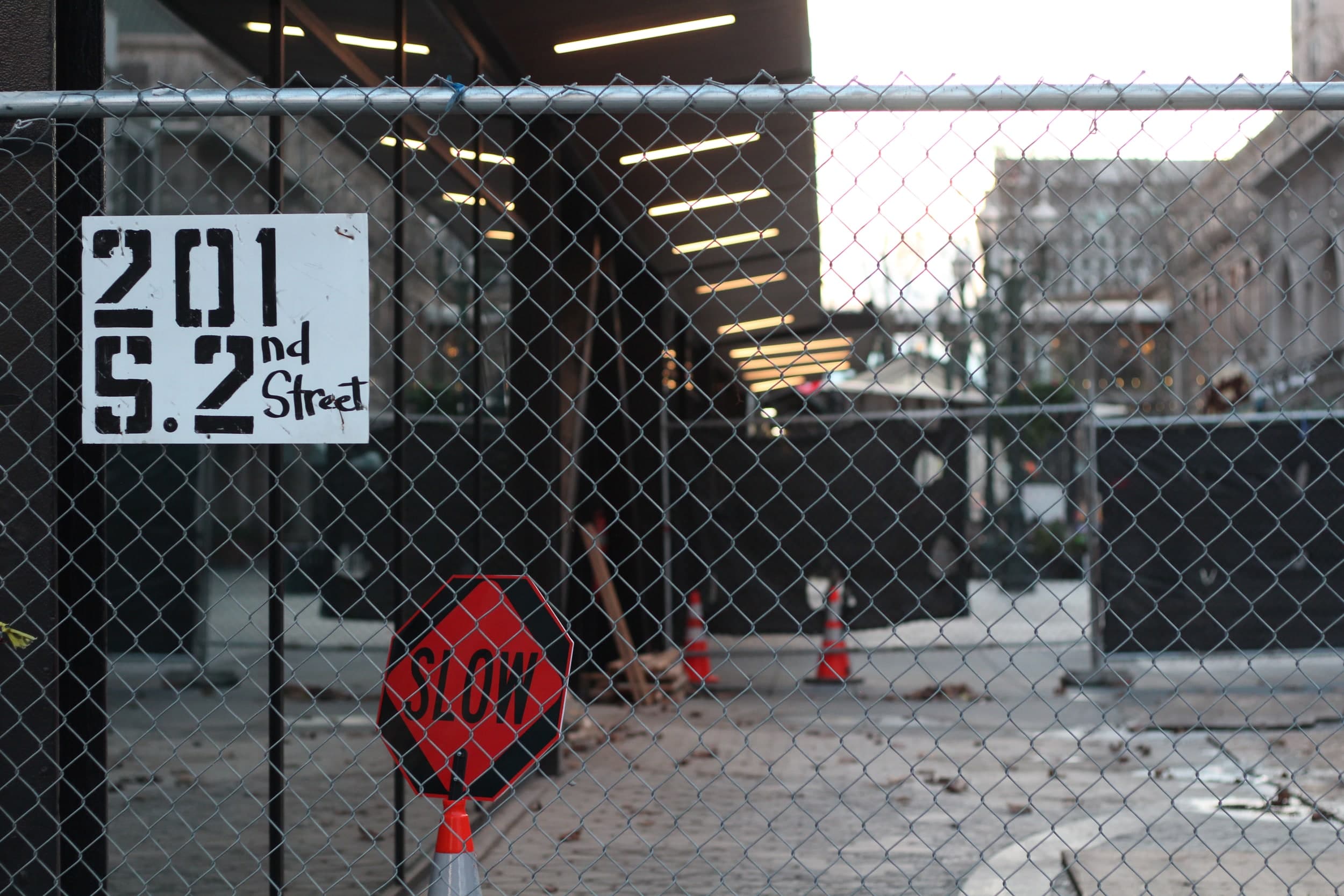 A SLOW sign and a hand-painted 201 S. 2nd Street sign on a chain-link construction fence
