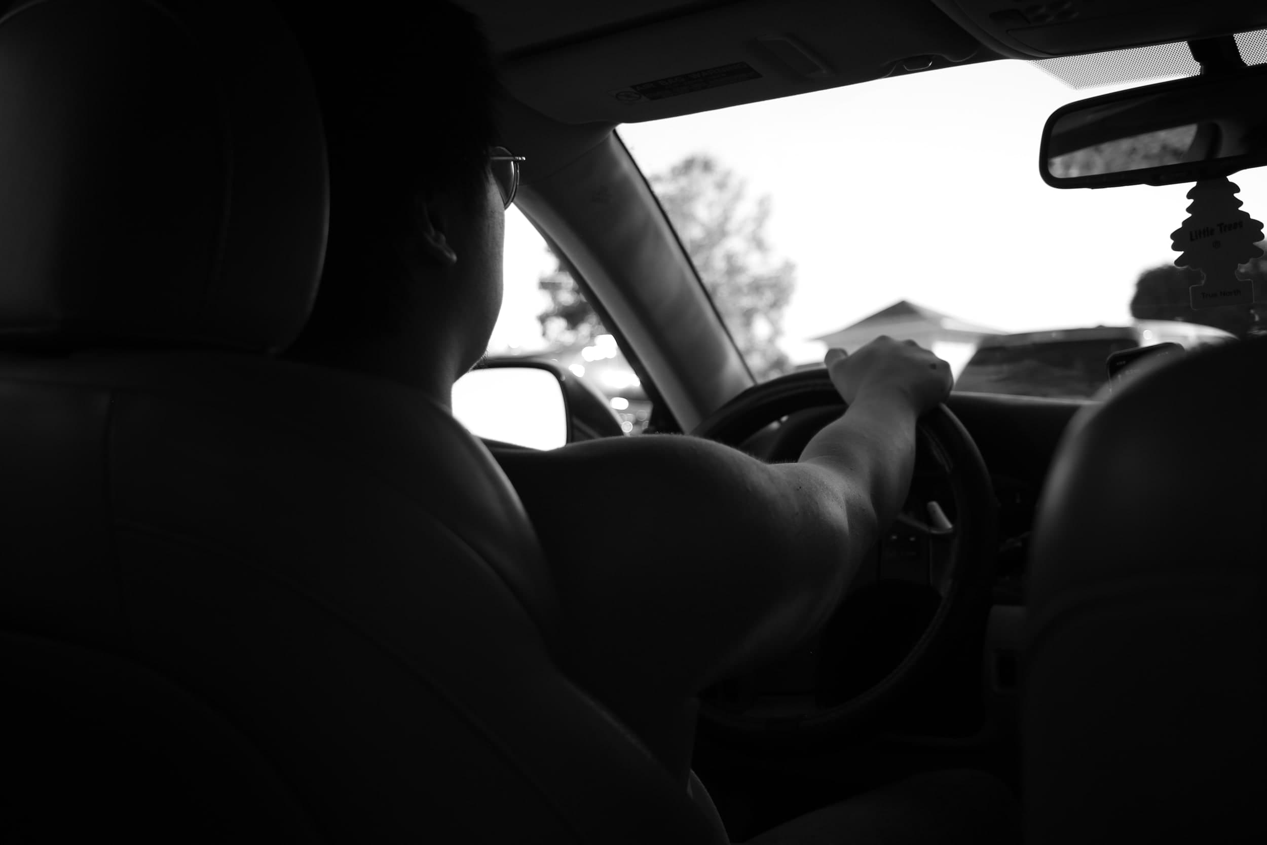 Black-and-white photo from the back seat of a person driving a car