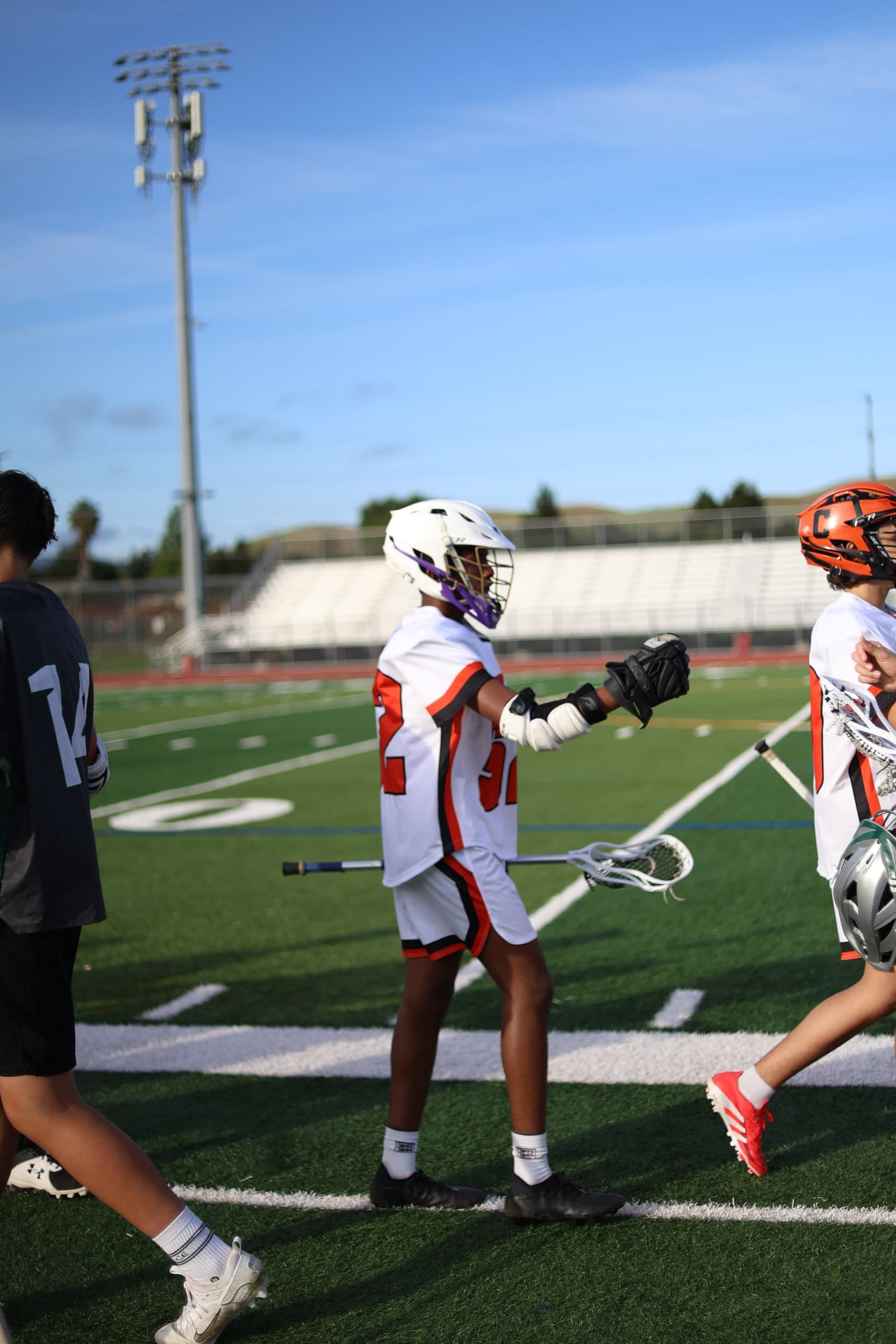 A lacrosse player in a white and orange number 32 jersey walking across the field
