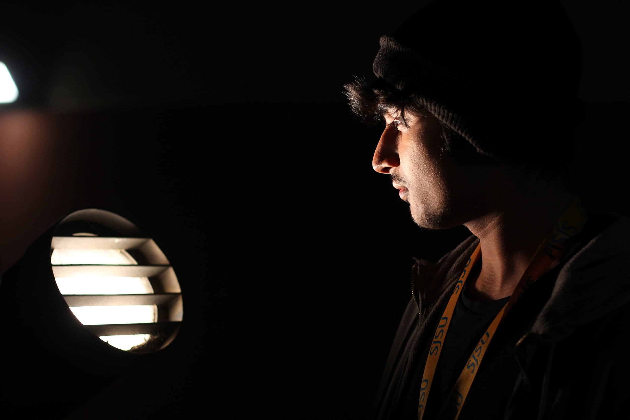 Profile of a person in a beanie lit by a single outdoor lamp at night