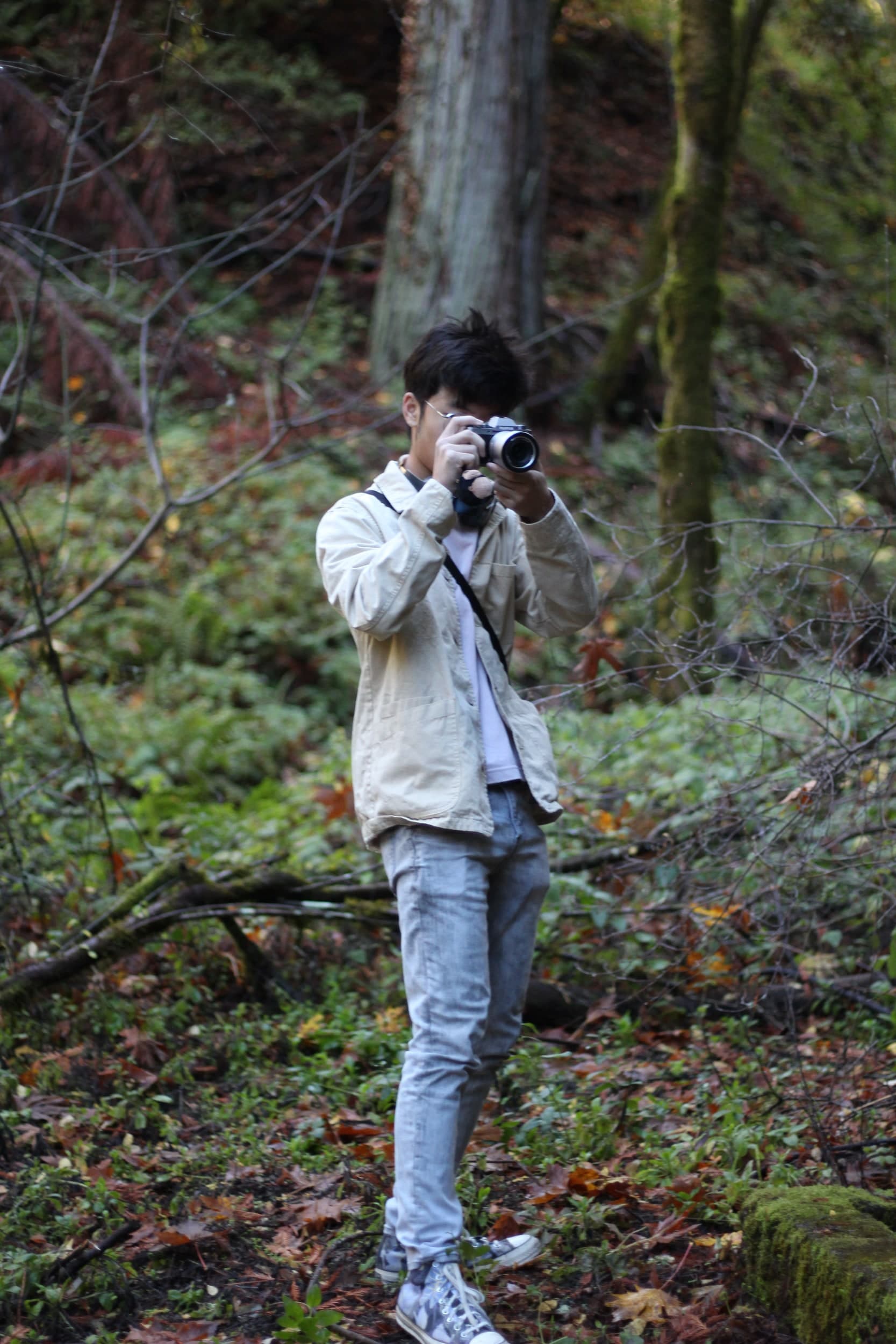 A person in a light jacket taking a photo with a camera in a forest
