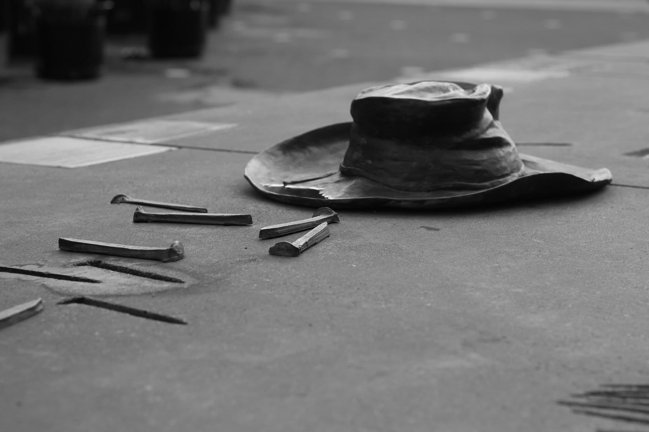 Black-and-white photo of a sculpted hat and railroad spikes set into a sidewalk